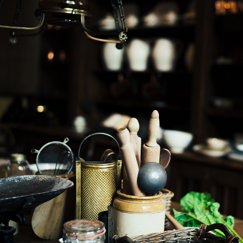 A clay jar with a metal ladle and wooden kitchen implements in an out-of-focus kitchen.
