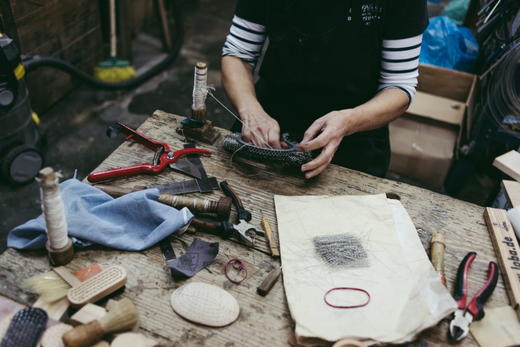 A white person working at a crafting bench, surrounded by pliers, brushes, wire, and snips.