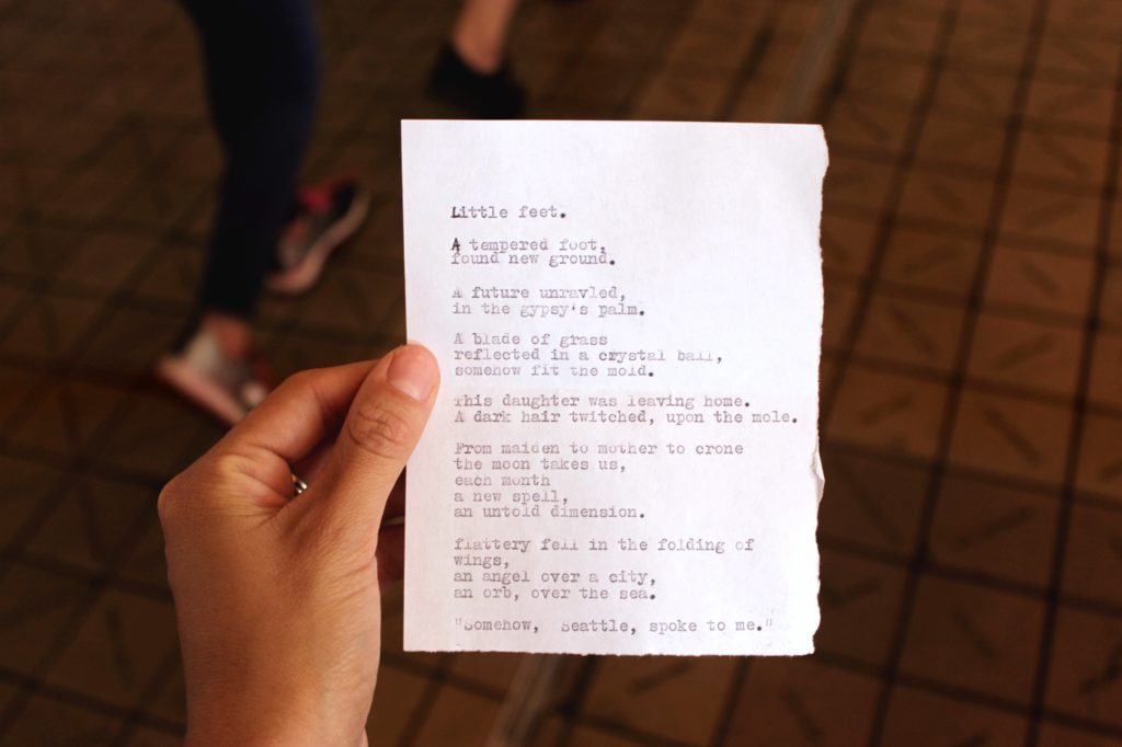 A Caucasian hand holding a small sheet of paper with a typewritten poem.