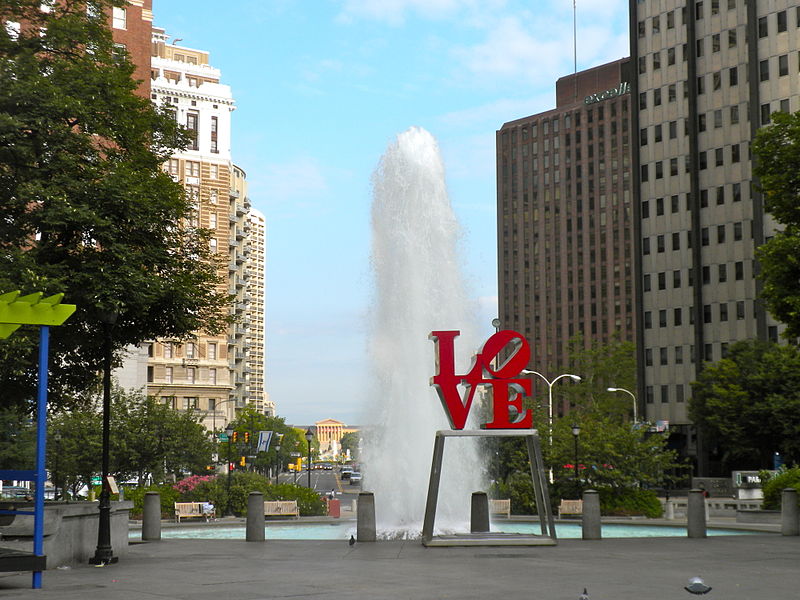 The LOVE statue in Philadelphia in front of a fountain on a clear summer day, with the Philadelphia Art Museum in the far distance.