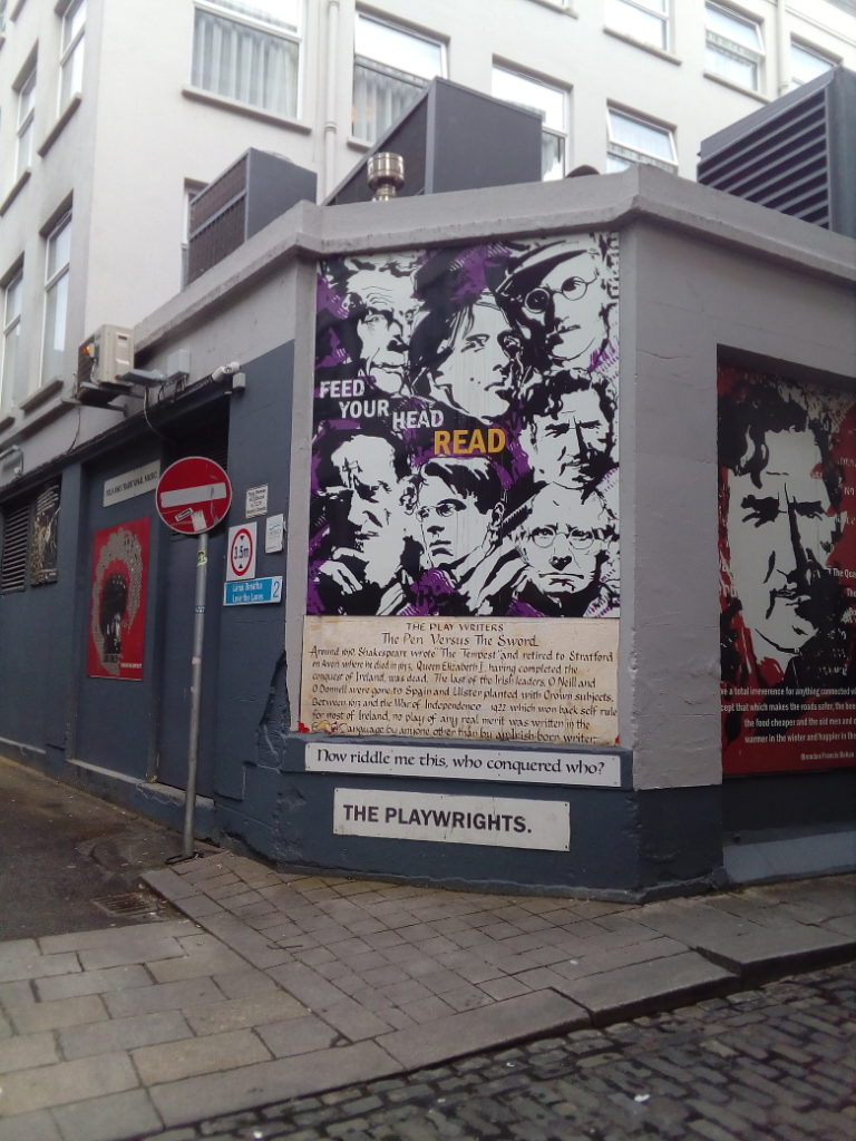 Street art with high-contrast black and white portraits of Irish writers on a purple background, with text that says "Feed your head: read."