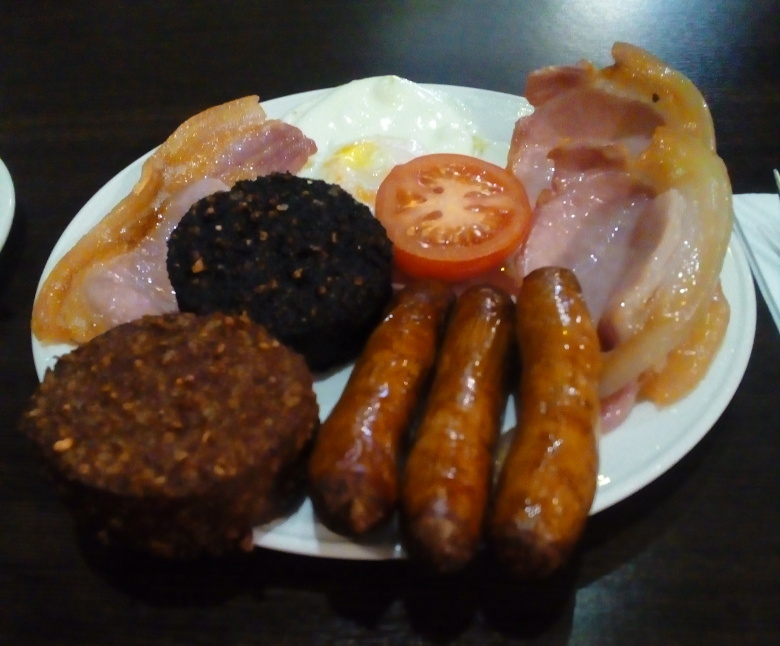 An Irish breakfast: sausages, bacon, ham, and half a tomato.