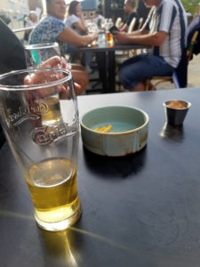 An askew view of two half-empty beers and a small blue bowl of French fries on a black table.
